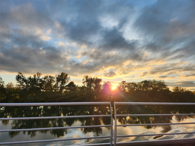 Sunset behind trees with reflections on the water.