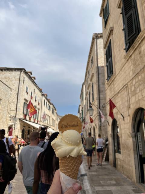 Ice cream cone held in front of a scenic street setting.