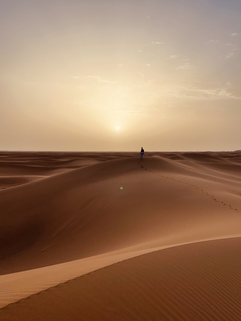 A lone person walking on sand dunes during sunset.