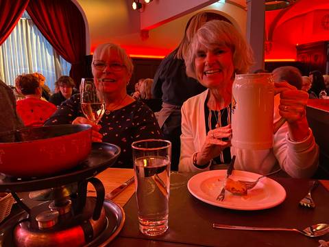       Older women enjoying a meal with large beer mugs in a cozy setting.
  