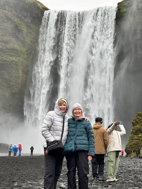 People posing in front of a large waterfall in a cold environment.