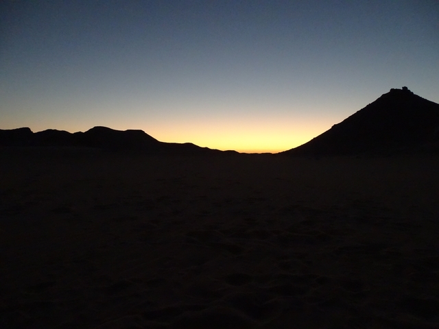       Sunset over a desert with silhouettes of hills.
  