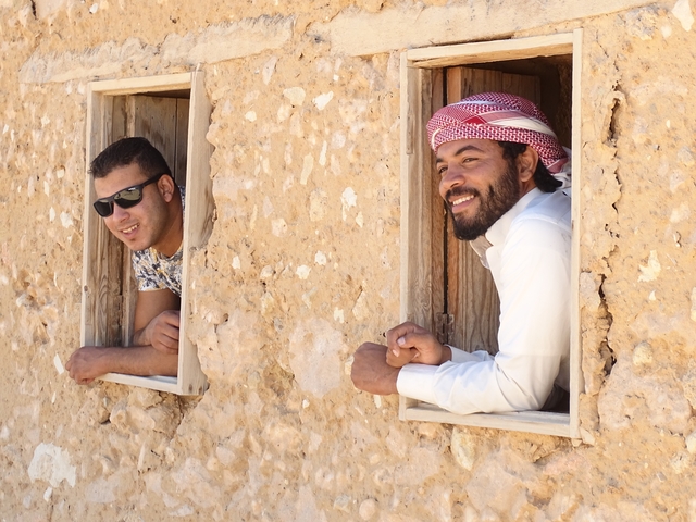       Two men leaning out of windows in a rustic adobe building.
  