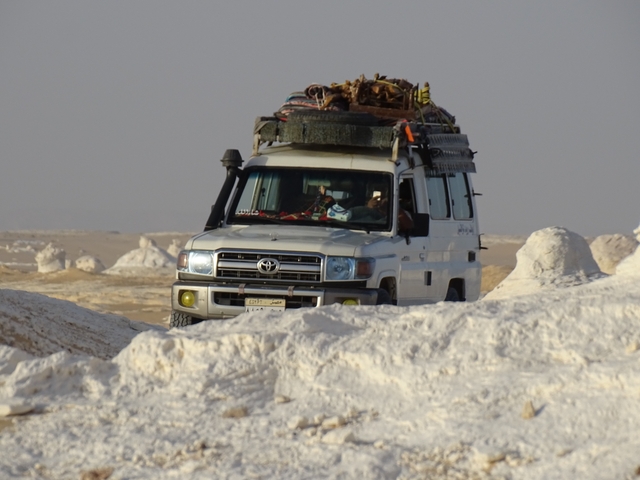       Vehicle driving through a desert landscape with white rock formations.
  
