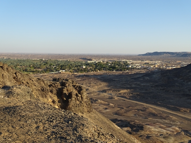       Desert landscape with distant greenery visible across the horizon.
  