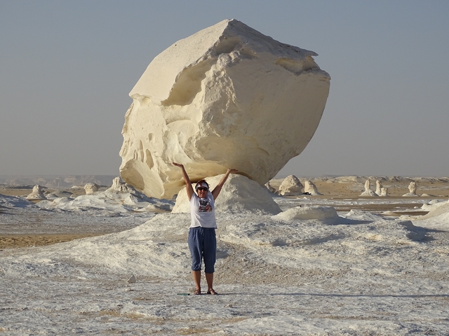       Person posing with arms raised next to a large white rock formation.
  