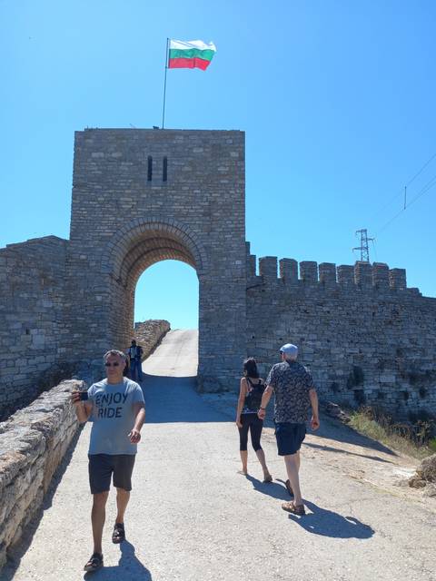 Stone gateway with people walking, a flag flying above.