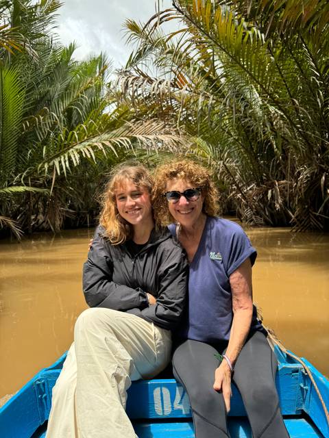 Two women sitting on a small boat amidst tropical greenery, smiling.