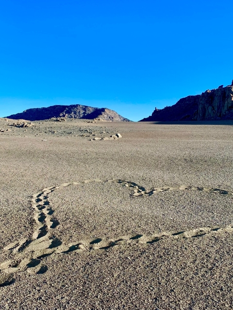       Footsteps imprinted on a flat sandy area with rocky hills.
  