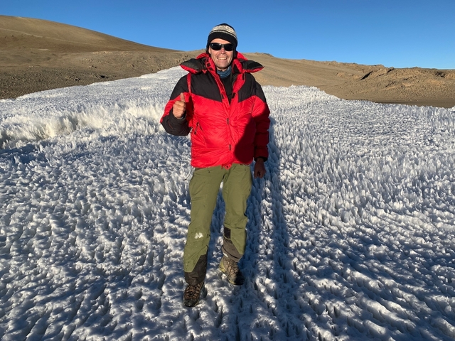       Person standing on a snowy terrain with mountainous background.
  