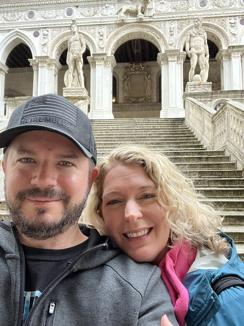 Two people posing on stone steps with columns in the background.