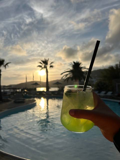 Hand holding a drink with poolside sunset.