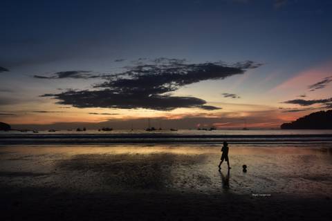 A child playing with a ball on a beach at sunset.