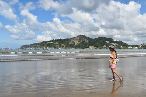 A person walking near the beach with hills in the background.
