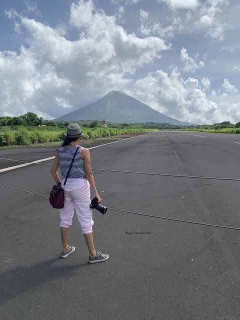 A person standing on an airport runway with a large volcano in the background.