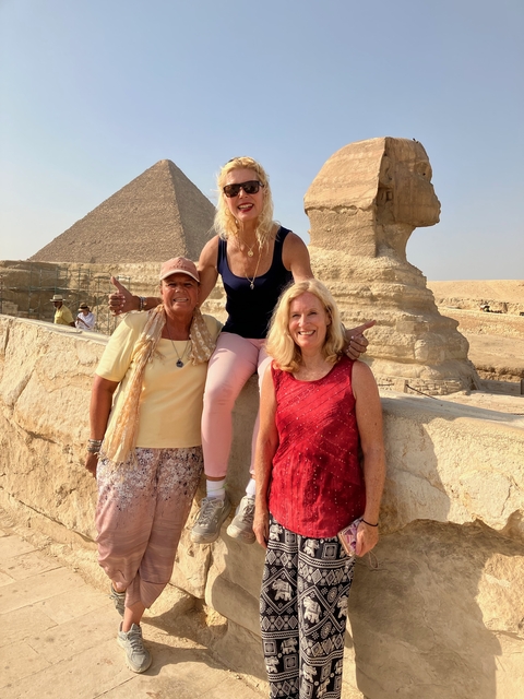 Three women posing in front of the Sphinx with pyramids in the background.