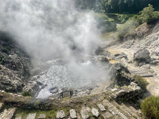       Steam rising from hot springs in a rugged terrain.
  