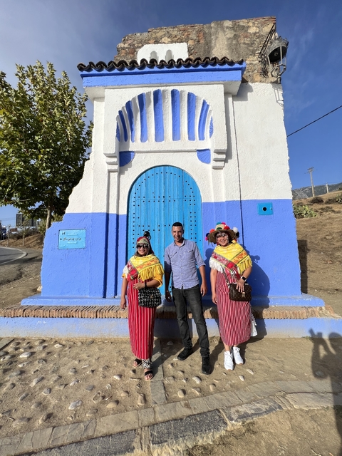       Three people in traditional attire in front of a blue and white building.
  