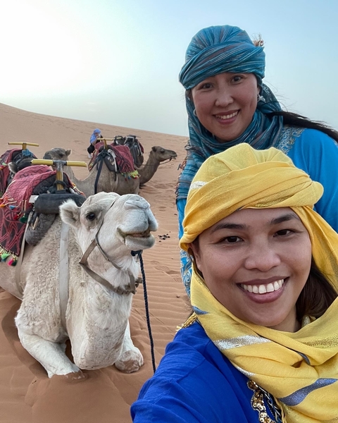 Smiling women with camels in the desert.