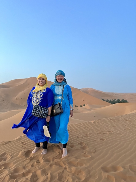 Two people in traditional clothing in a desert landscape with sand dunes.