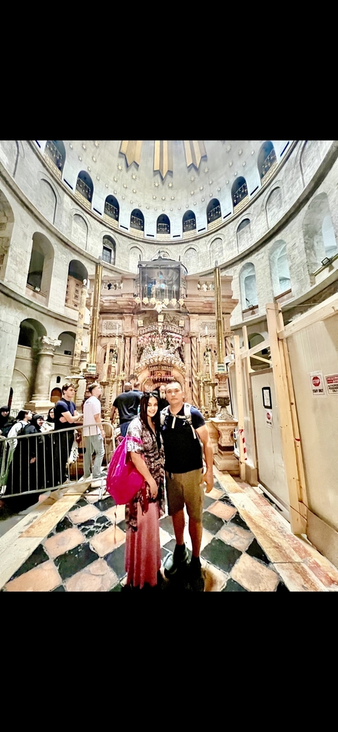       Two people posing in an ornate interior space with arches and gold decorations.
  