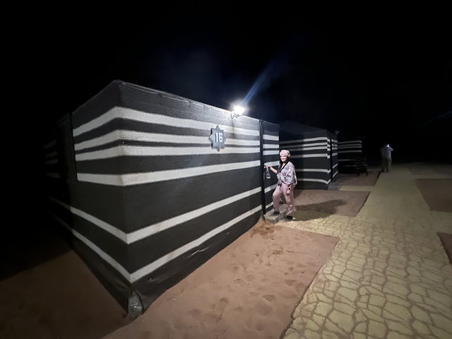       Person standing next to a striped bedouin tent at night.
  
