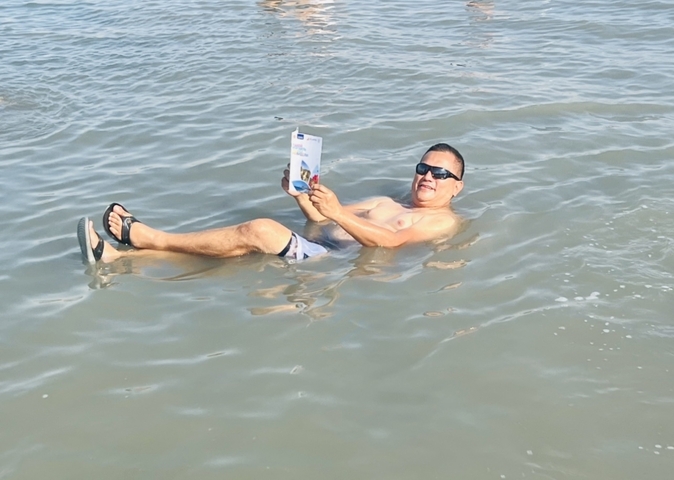 Man floating in water holding a magazine.