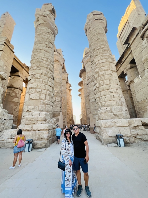       Two people posing amid large stone pillars of an ancient structure.
  