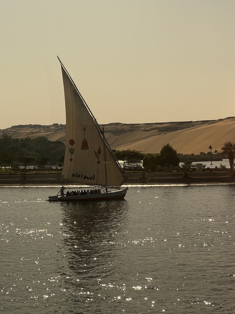       Sailboat with decorations on a river with dunes in the background.
  