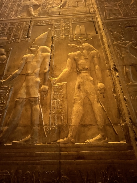 Carvings depicting figures on a historic wall, warmly illuminated.