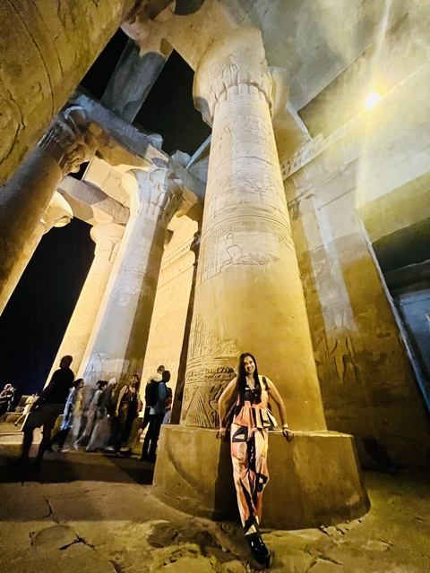       Person posing with illuminated ancient columns at night.
  