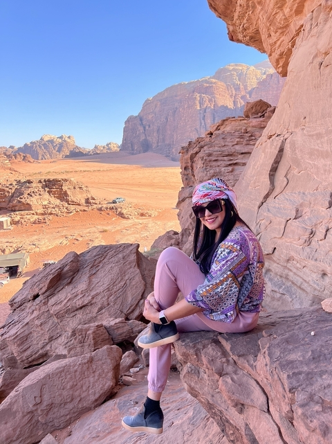 Person sitting on rock formations in a desert landscape.