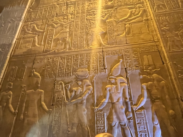       Wall with hieroglyphs and carved figures, warmly lit.
  