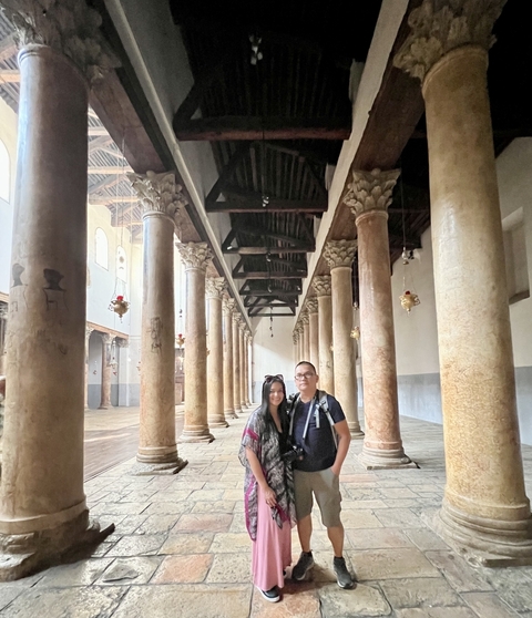 Two people posing among ancient columns inside a historic site.