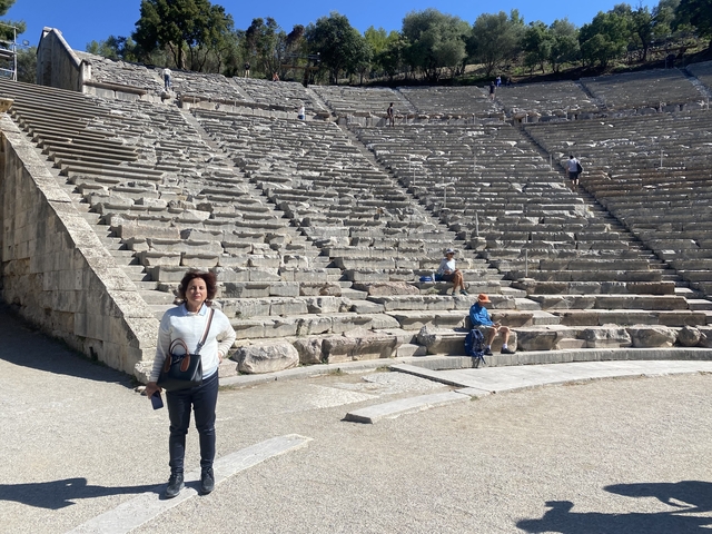       A person in front of an ancient amphitheater with others seated.
  