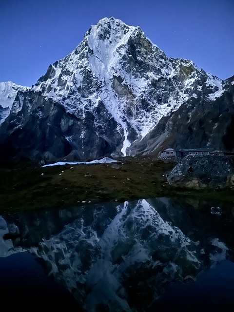       Snow-covered mountains with a building at their base, reflecting in a lake at dusk.
  