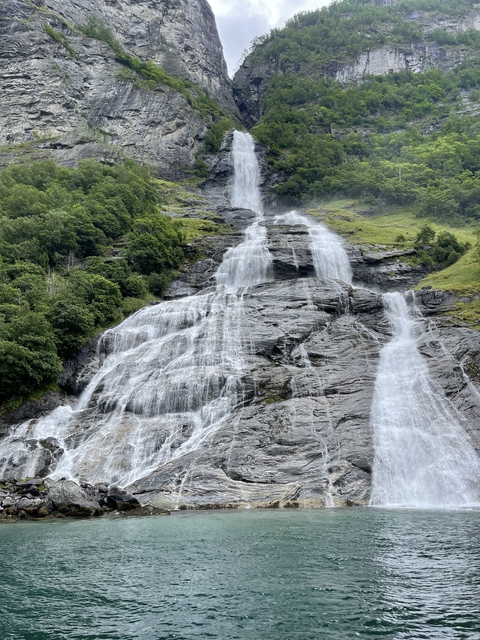 A waterfall flowing down a rocky face with green surroundings.