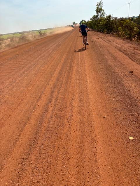 Cyclist on a red dirt road under a clear sky.