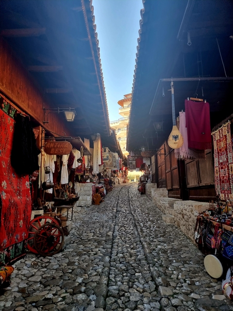 Cobblestone street lined with market stalls and colorful textiles.