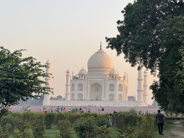 The Taj Mahal behind trees with people in the foreground.