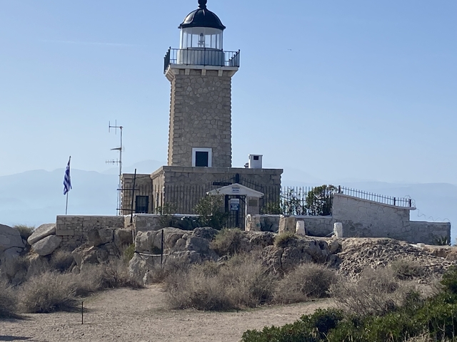 A lighthouse with a Greek flag on a rocky hill.