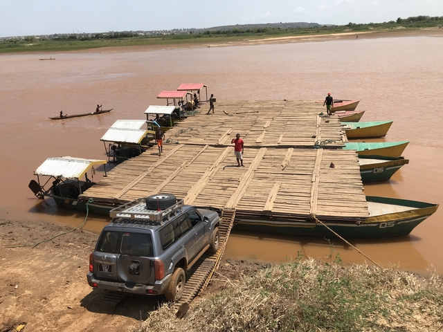       A river crossing with cars and people.
  