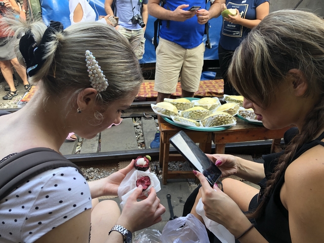 Two women sitting at a market with fruit and a mobile phone.