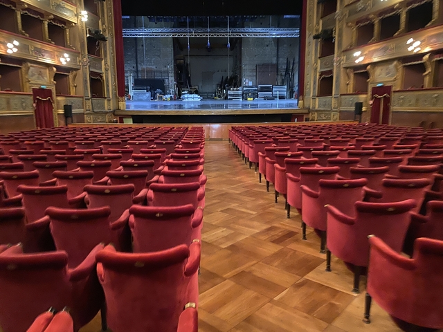       View of an empty theater with red seats facing the stage.
  