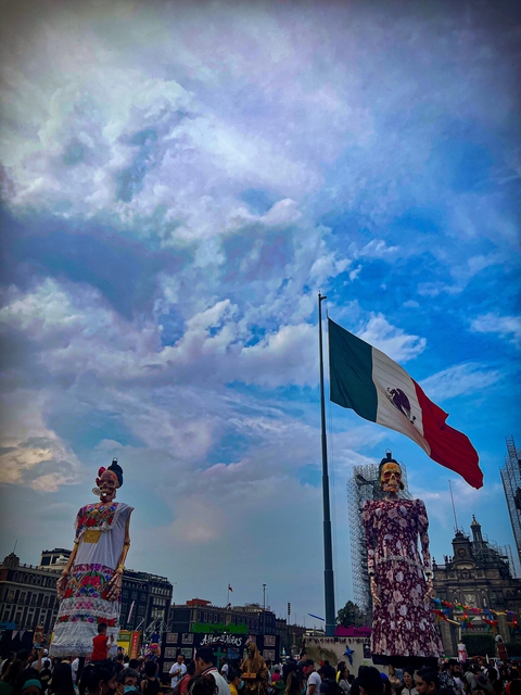 Large Mexican flag waving against a blue sky.