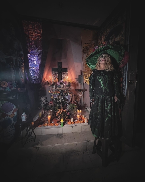 Person in costume next to an altar with candles for Day of the Dead.