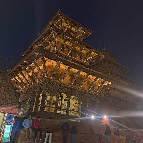 Illuminated traditional building at night with people around.