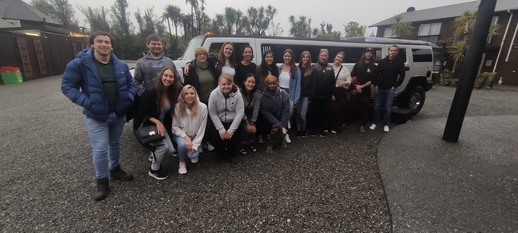       A large group of people posing together in front of a limousine.
  