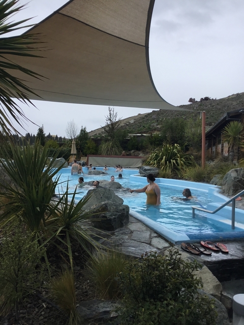      People enjoying a hot spring pool with mountains in the background.
  