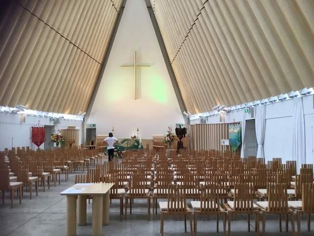       An interior view of a modern church with wooden chairs.
  